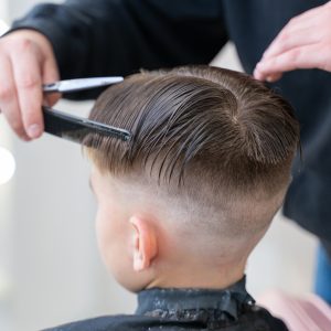 The hairdresser makes a boy's haircut with a clipper